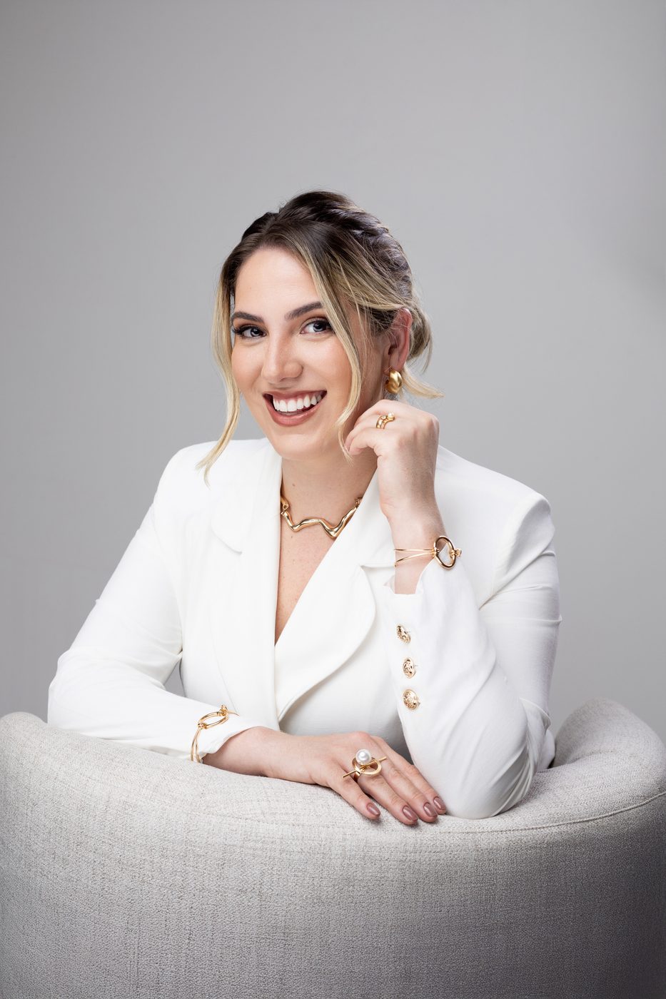 Laysses Sanches de blazer branco, sentada, sorrindo